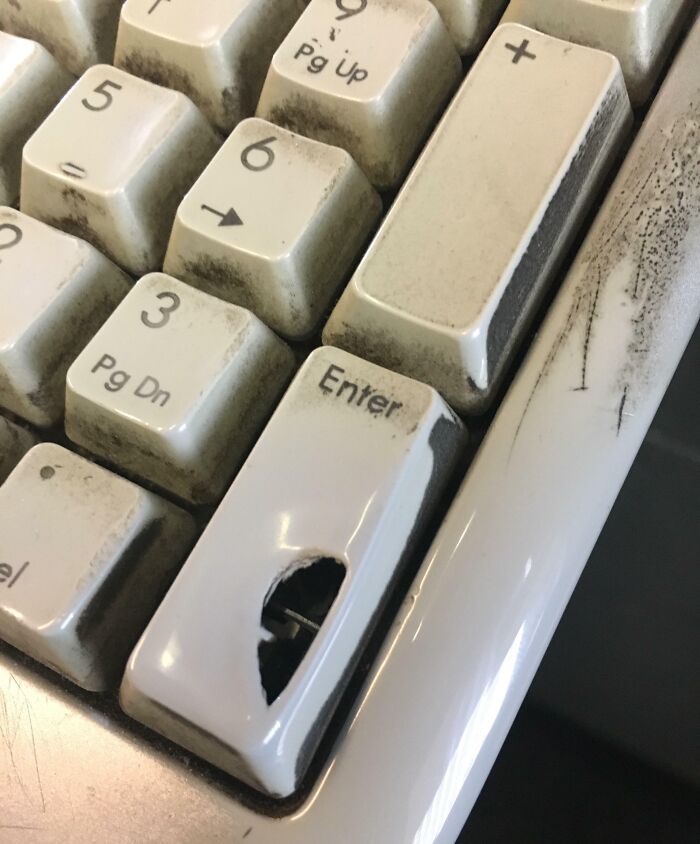 A worn keyboard with a hole in the Enter key, showcasing transformation by time and use.