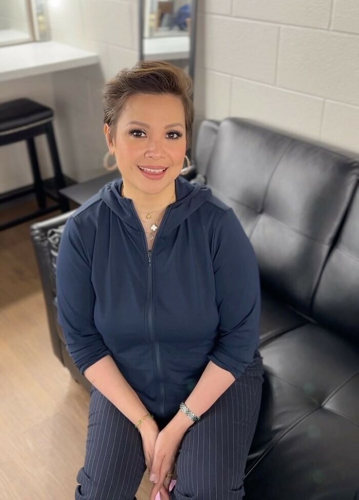 Person seated on a black couch, wearing a navy hoodie and striped pants, smiling in a classy manner.