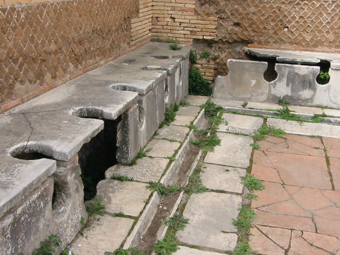 Roman Empire public latrines made of stone with multiple seats, showcasing ancient sanitation engineering.