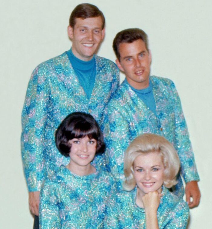 Four people in matching blue outfits, showcasing vintage hairstyles with unique flair from yesteryear.