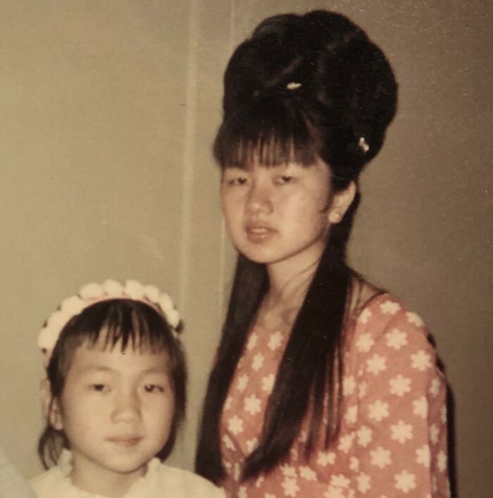 Two girls with unique yesteryear hairstyles; one with a tall updo and floral dress, the other with floral headband.