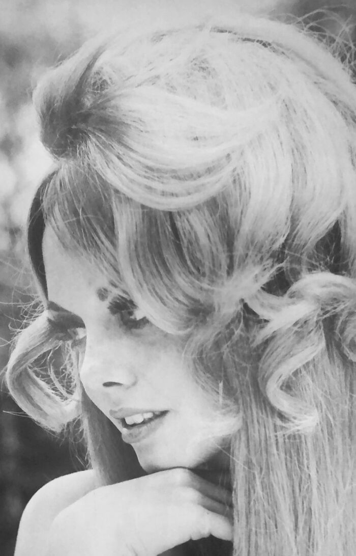 Black and white photo of a woman with an elaborate, voluminous hairstyle from the past.