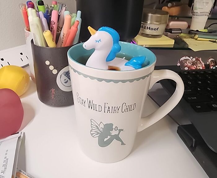 Unicorn pool float in a mug with office supplies on a desk.