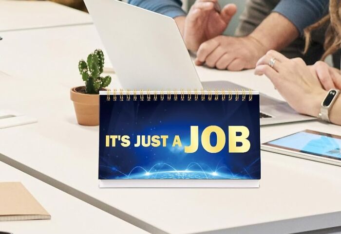 Desk scene with a motivational sign reading "It's just a job" to ease work stress.