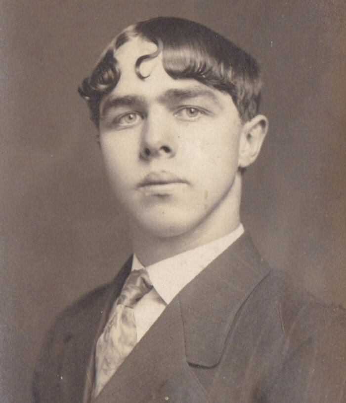 Vintage portrait of a man with a unique curled hairstyle from yesteryear, wearing a suit and tie.