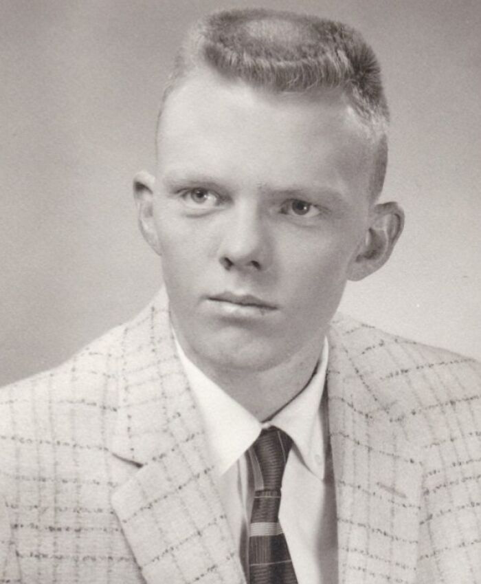 Black and white photo of a man with unique yesteryear hairstyle, wearing a plaid suit and tie.