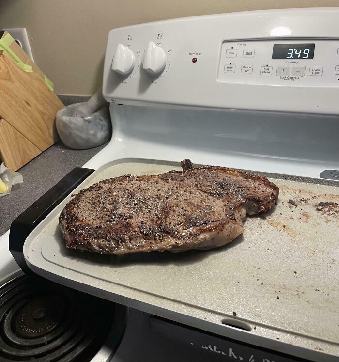 Giant steak humorously cooked on a stovetop, showcasing how men make life amusingly unpredictable.