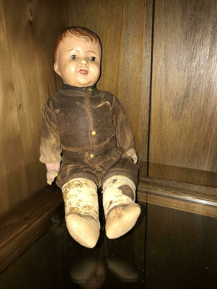 Creepy antique doll with faded clothes sitting in the corner of a wooden cabinet, found hidden in a home.