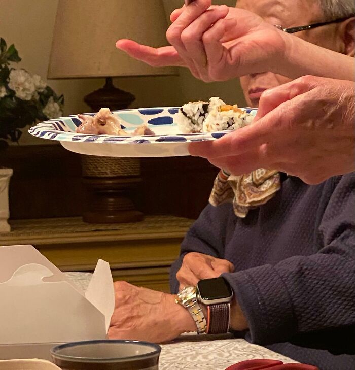 Elderly person humorously pointing at sushi on a plate, wearing a smart watch at the table.