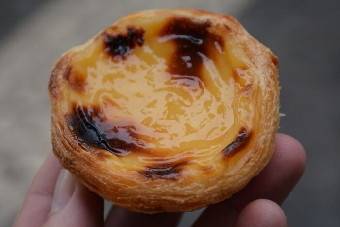 A hand holding a Portuguese custard tart, a top dish from different countries, with a golden, caramelized top.