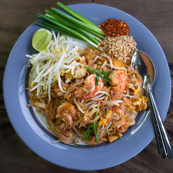 Pad Thai served with shrimp, bean sprouts, peanuts, and lime on a blue plate, representing a top dish from different countries.
