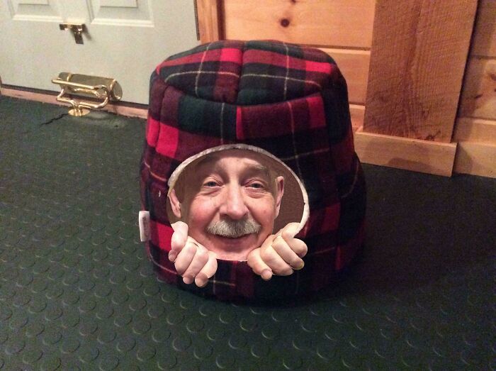 Elderly man playfully peeking from a plaid cat house, showcasing humor and creativity.
