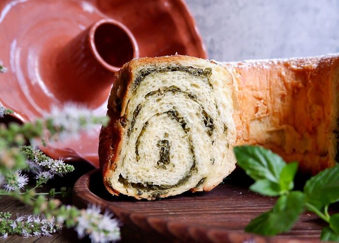 Slice of traditional bread from different countries, featuring a spiral herb filling, displayed on a wooden board.