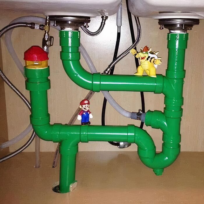 Funny image of green pipes under a sink with Mario and Bowser figurines, resembling a game level.