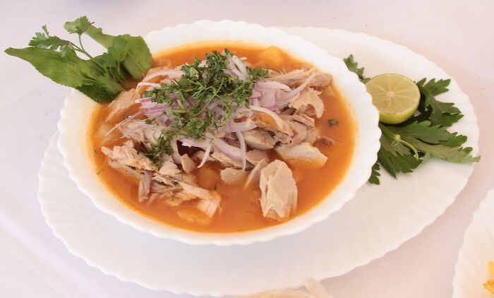 Top dish from different countries, featuring a savory soup with chicken, herbs, onions, and lime garnish.