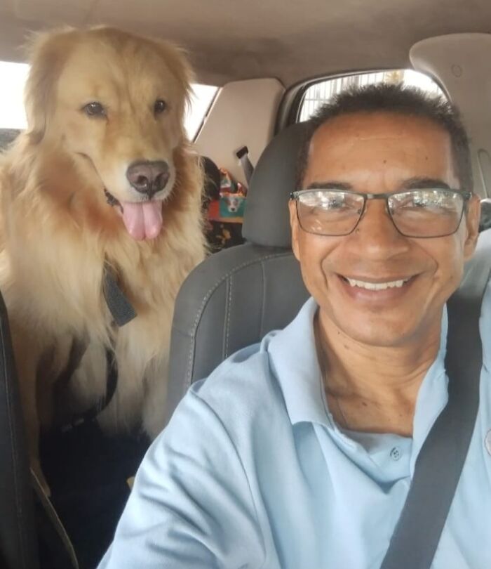 Man smiling with a Golden Retriever in the pet taxi, both enjoying a ride.
