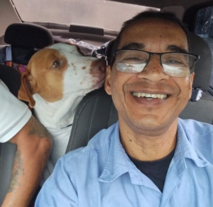 Man smiling in a pet taxi selfie with a dog in the backseat, both enjoying the ride.