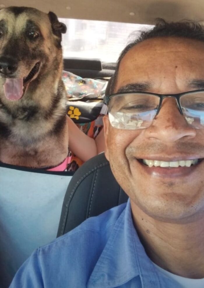 Man taking a selfie in his pet taxi with a smiling dog passenger.