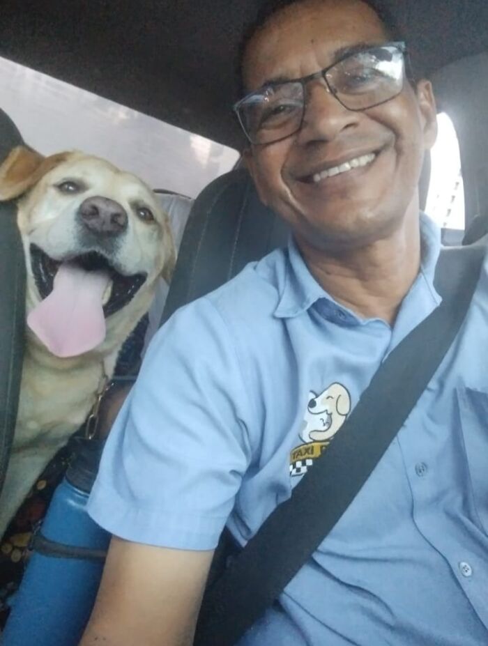 Smiling pet taxi driver takes a selfie with a happy dog in the backseat, both enjoying the ride.
