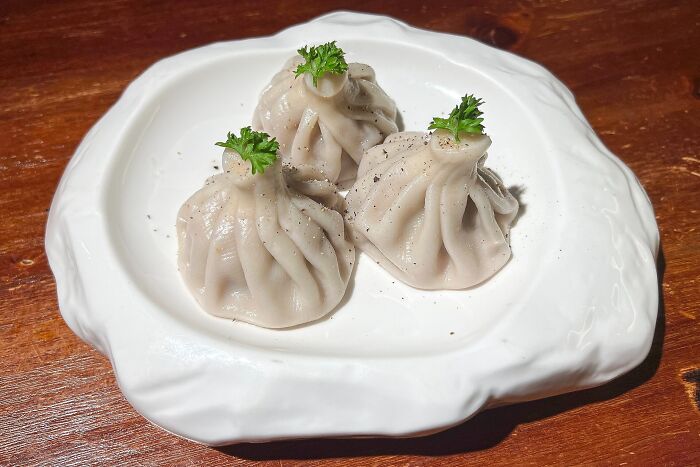 Three dumplings garnished with parsley on a white plate, representing a top dish from different countries.