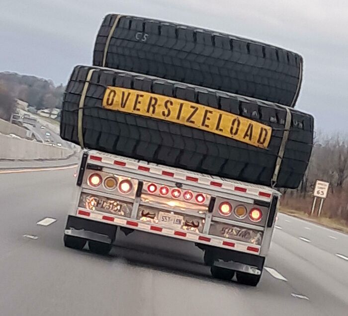Oversized load truck carrying massive tires on a highway, looking surreal but real.