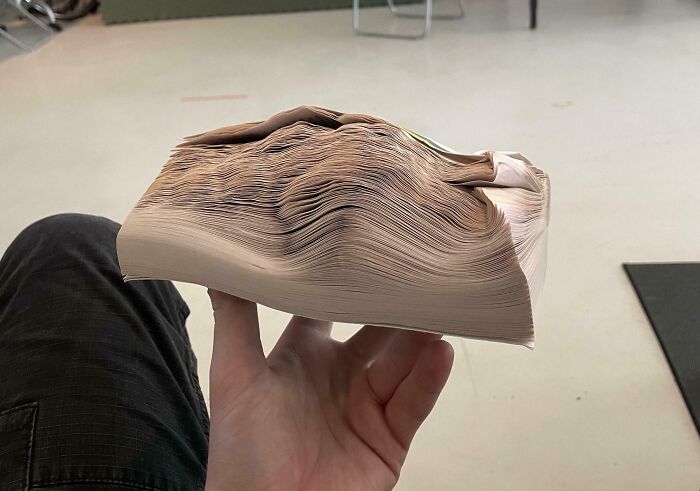 A warped book clutched in hand, appearing fake but real, illustrating physics and optical illusion.