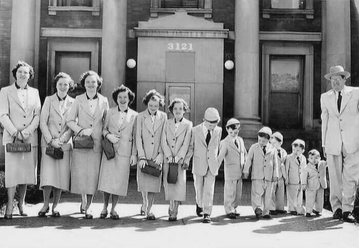Group of people in matching suits lined up by height in front of a building, illustrating fascinating old images.