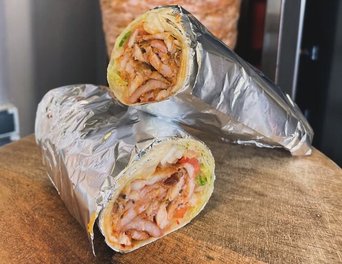 Wrap sandwich filled with seasoned meat and veggies, featured dish from different countries, resting on a wooden surface.