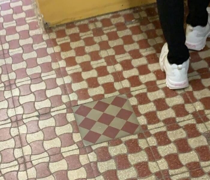 Failed repair attempt with mismatched floor tile pattern next to person's feet.
