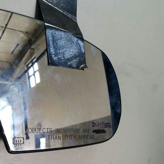 Side mirror with "dumber" humorously written instead of "closer," showing funny coworkers' creativity.