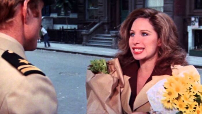 Woman holding flowers, talking to a man in uniform, in a scene from a tear-jerker movie.