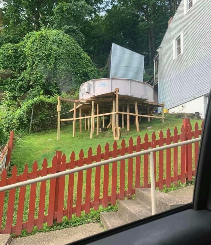 Failed repair attempt with a DIY pool on unsteady wooden supports in a yard with a red fence.