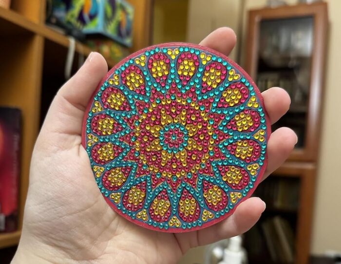 Colorful glittery mandala-like design held in hand, featuring vibrant pink, yellow, and turquoise patterns.