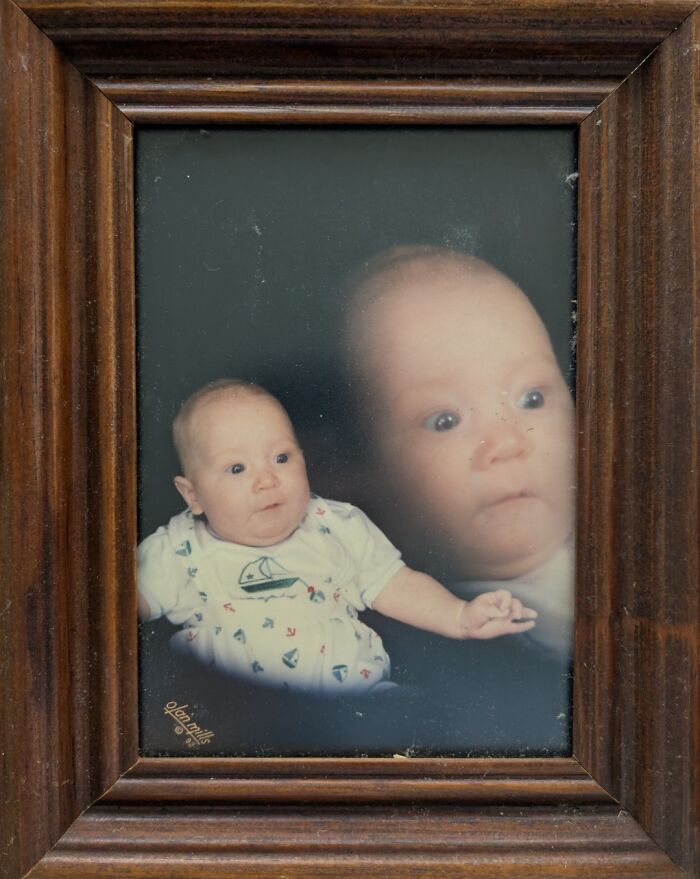 Baby with humorous expression in wooden frame, showcasing funny photography.