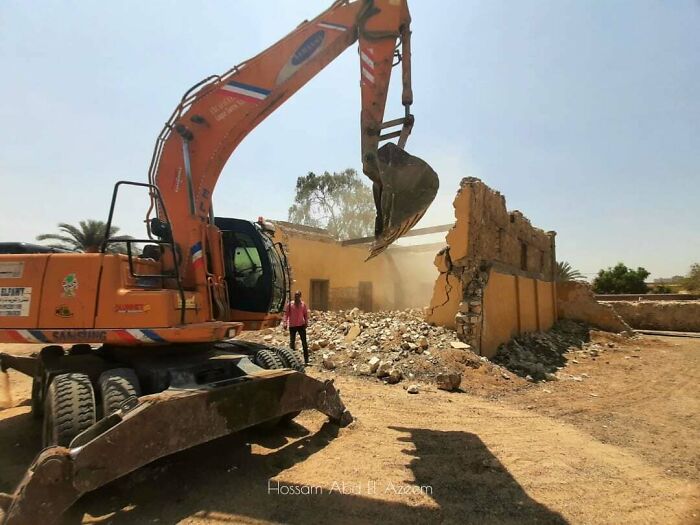 Excavator demolishing a building as a person watches, capturing an online-worthy moment of frustration turned action.
