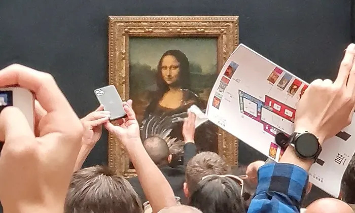 Crowd taking photos of the Mona Lisa, focusing on capturing the iconic painting.