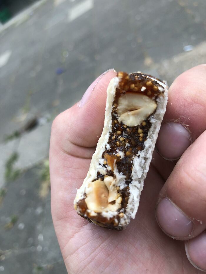 Hand holding a bitten snack bar with nuts and seeds, a moment captured from an online post expressing frustration.