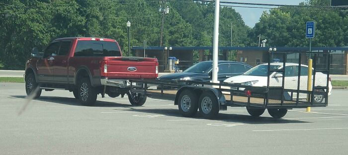 Red truck with a trailer parked across two spaces in a parking lot, blocking other vehicles.