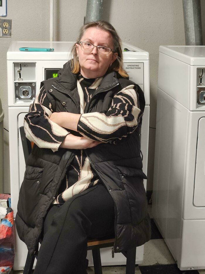Woman looking displeased with crossed arms, sitting in a laundromat setting.