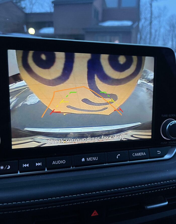 Backup camera displaying a large funny face, illustrating coworkers' humor in a car safety message.