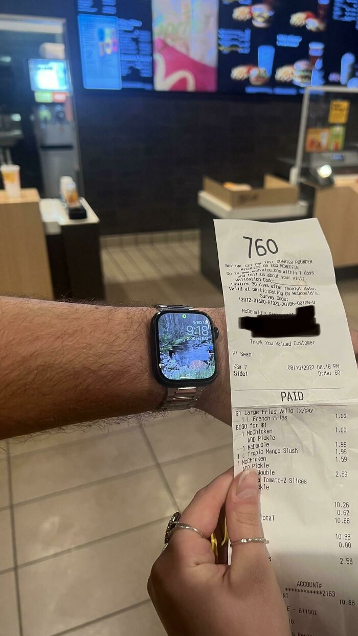 A person holding a receipt at a fast-food counter, showing an Apple Watch displaying 9:18, expressing frustration online.