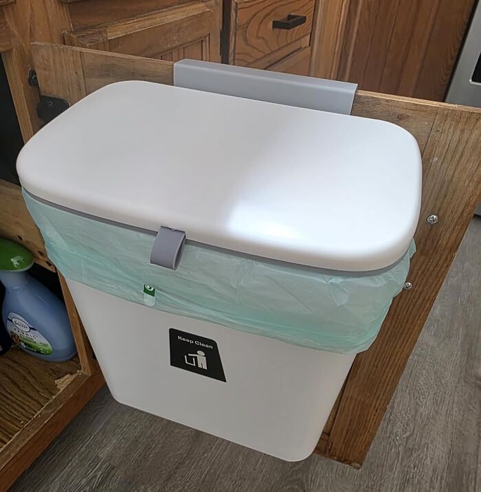 Hanging white trash bin inside a wooden cabinet door, perfect for solo living essentials.
