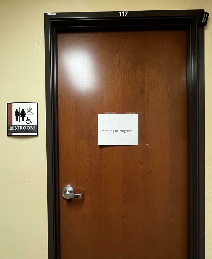 "Restroom door with 'Meeting In Progress' sign, showcasing funny coworkers' humor."
