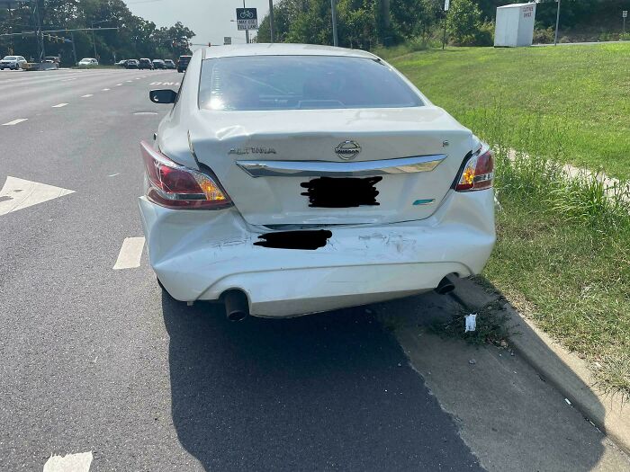 Damaged white car parked on the side of the road, showing rear-end collision impact.