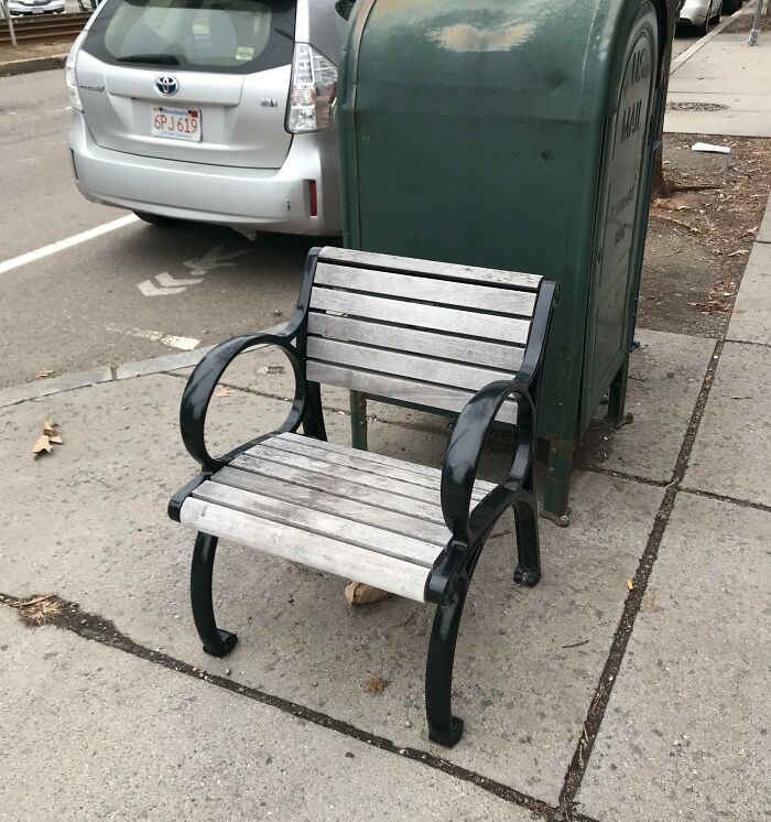 Bench oddly placed in front of a mailbox on a city sidewalk, looking staged but real.