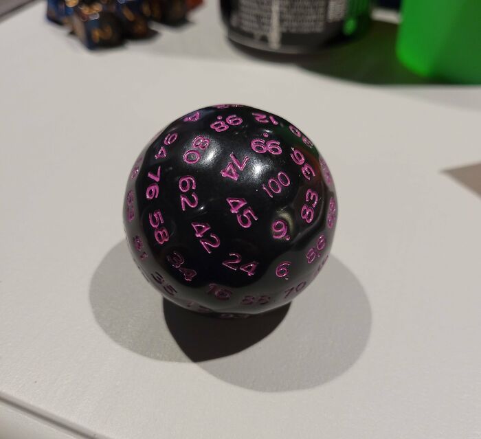 Black sphere with pink numbers resembling a dice, creating an optical illusion effect on a tabletop.