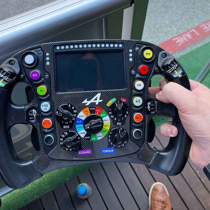 Hand holding a complex steering wheel, full of colorful buttons and knobs, appearing fake but actually real.