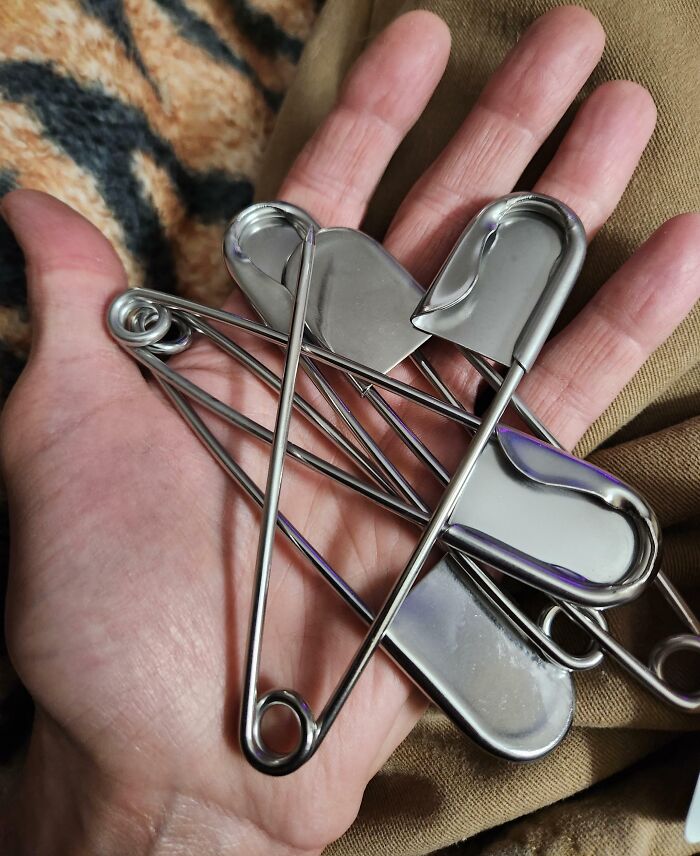 Close-up of giant safety pins in a hand, creating an illusion of oversized objects that look fake but are real.