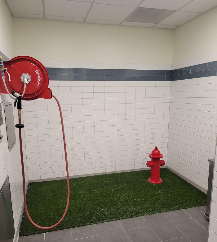 Red fire hydrant and hose reel inside a tiled room, with grass patch, looking fake but real.