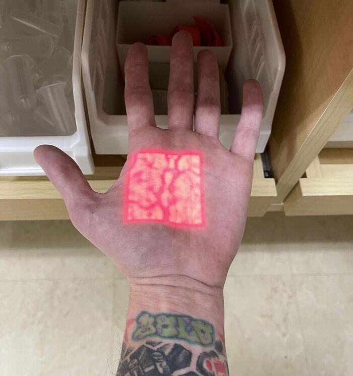 Tattooed hand with red pattern light projection, creating a fake yet real optical illusion.